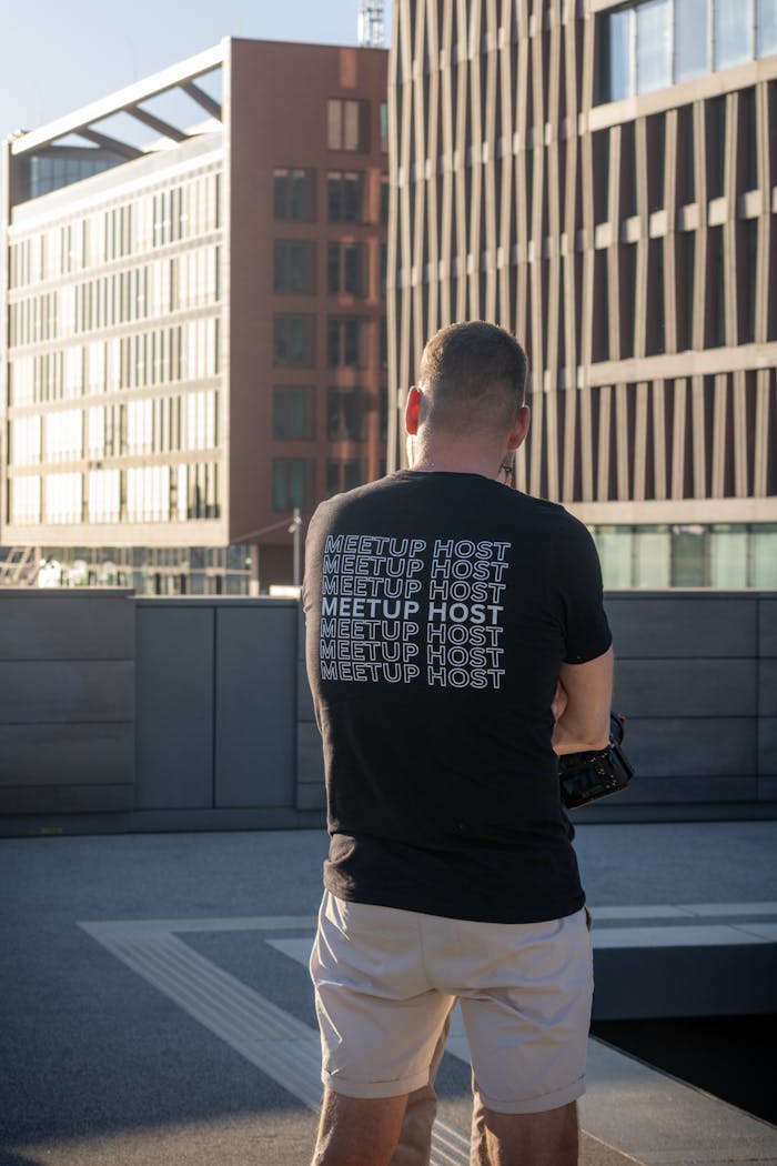 A man wearing a 'Meetup Host' t-shirt in Hamburg's modern urban landscape during daylight.