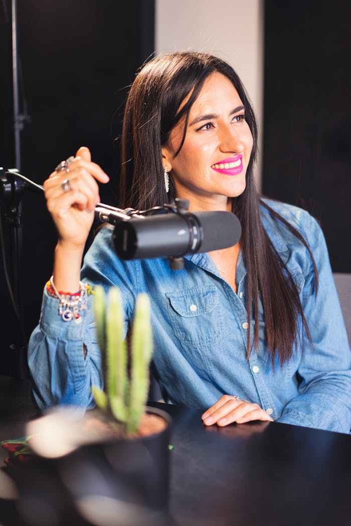 Cheerful woman podcast host in recording studio with microphone and denim shirt.